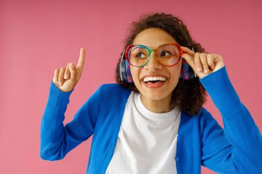 Pozitif gülümseyen kadın model, pembe stüdyo arka planındaki tanıtım teklifinden etkilenmiş görünüyor.