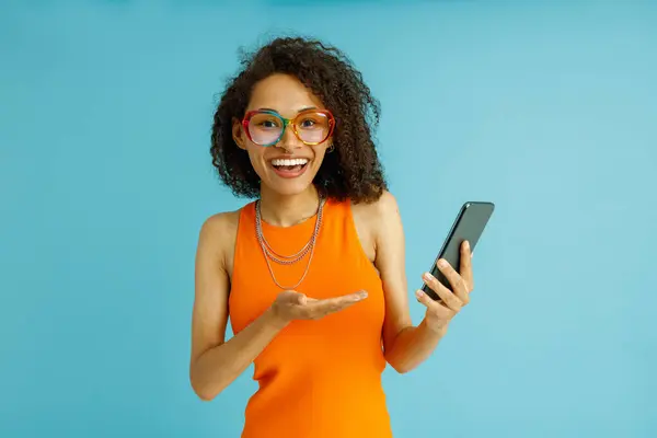 Красива Жінка Окулярах Вказує Мобільний Телефон Стоїть Синьому Студійному Фоні Ліцензійні Стокові Фото