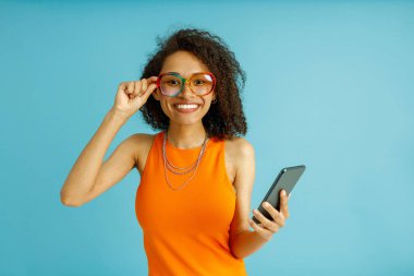 Mavi stüdyo arka planında dururken cep telefonu tutan olumlu kadın.