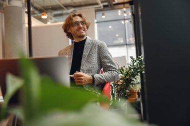 Laptop üzerinde çalışan yakışıklı girişimci iş günü boyunca modern iş yerinde oturuyor.