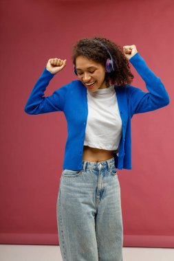 Kırmızı stüdyo arka planında el kaldırarak dans eden kulaklıklı, gülümseyen kadın.