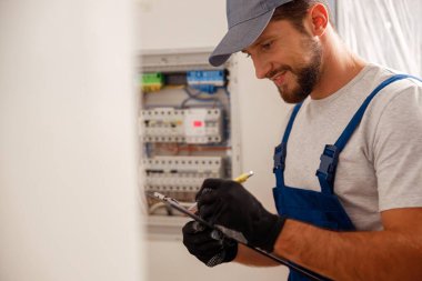 Elektrik teknisyenleri panoya yazmakla meşguller. Yerleşim yerindeki bir elektrik panelinden toplanan veriler. Bakım, meslek, güvenlik kavramı