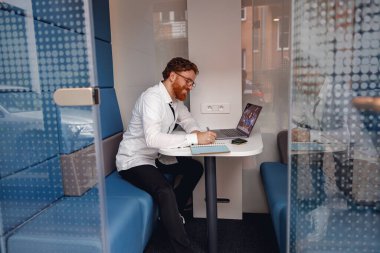 Erkek serbest çalışanın iş yerinde rahat otururken iş arkadaşıyla görüntülü bir konferansı var.