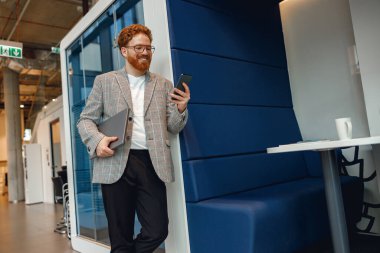 Bilgisayarı olan yakışıklı bir satış yöneticisi modern iş geçmişi üzerinde duruyor ve telefon kullanıyor.