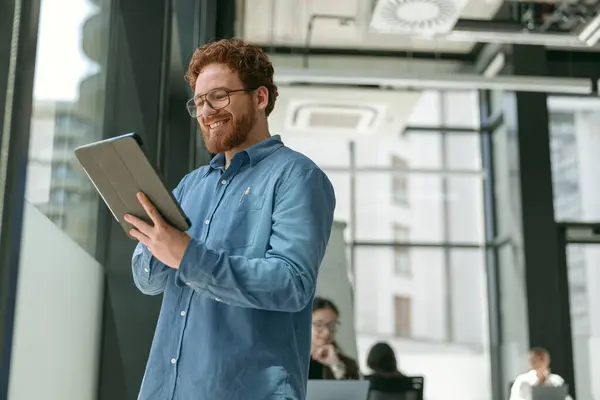 窓の近くにオフィスに立っている間 デジタルタブレットで働く笑顔のビジネスマン — ストック写真