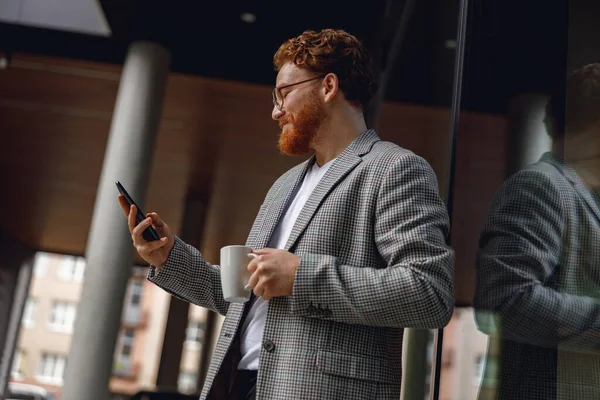 休憩時間中にオフィスの近くに立っている間携帯電話を保持するハンサムな男性フリーランサー — ストック写真