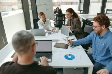 Bir grup genç iş adamı ofis masasında otururken bir şeyler tartışıyor ve gülümsüyor.