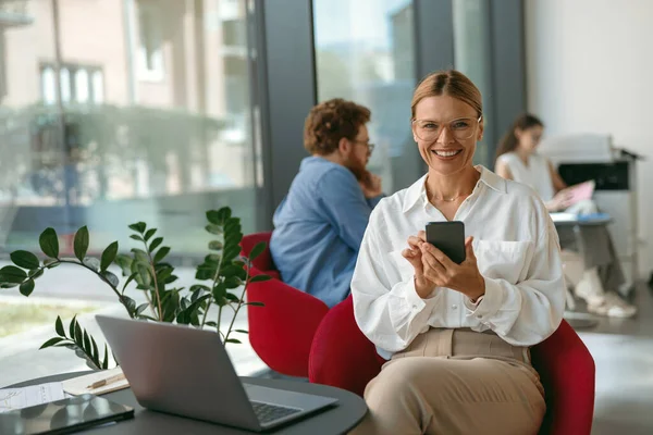 Geschäftsfrau Benutzt Handy Während Sie Büro Laptop Arbeitet Hochwertiges Foto lizenzfreie Stockbilder