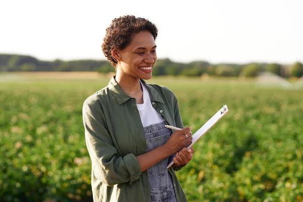 Woman agronomist making notes in clipboard while standing on vegetables farm background