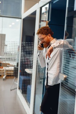 Gözlüklü, gülümseyen erkek yönetici modern çalışma alanında telefonla konuşuyor.