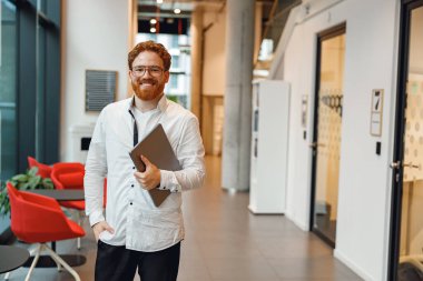 Modern çalışma arka planında dizüstü bilgisayarı olan yakışıklı bir satış müdürü ve kamera gibi görünüyor.