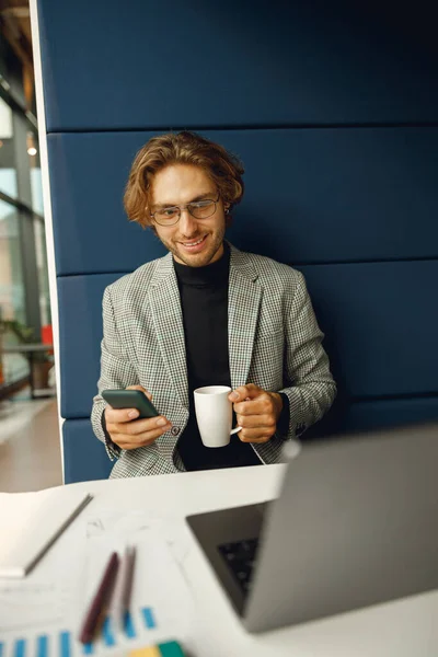 Businessman holding phone while sitting in coworking and working on laptop
