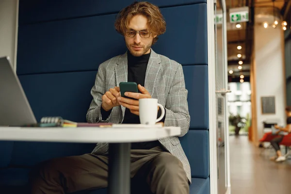 Focused businessman holding phone while sitting in office during break time. High quality photo