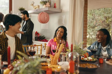 Bir grup gülen arkadaş evde Noel partisinde sohbet edip şarap içiyorlar.