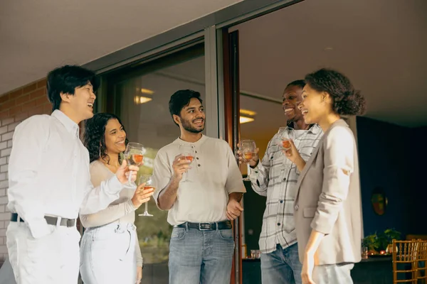 Group of smiling friends enjoying in conversation and drinking wine during holiday party at home