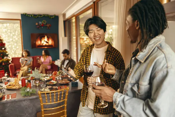 Group of smiling friends enjoying in conversation and drinking wine during Christmas party at home