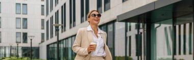 Kahveli gülümseyen kadın ofis çalışanı, teneffüste modern bina arka planında yürüyor.
