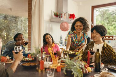 Bir grup gülen arkadaş evde Noel partisinde sohbet edip şarap içiyorlar.