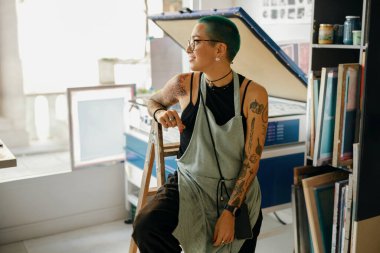 Tasarım stüdyosundaki baskı makinesinin arka planında oturan yaratıcı kadın işçi