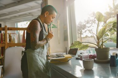 Önlüklü kadın işçi atölyede çalışırken not defterine ayrıntıları sıralar 