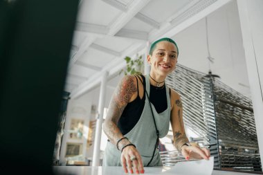 Önlüklü, gülümseyen bir kadın işçi atölyede baskı makinesi kullanıyor. Yüksek kalite fotoğraf