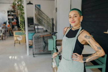 Tasarım stüdyosunun arka planında duran pozitif kadın çalışan ve gülümseyerek kameraya bakıyor.