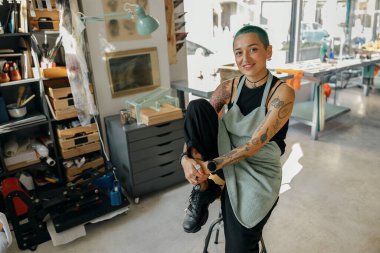 Yaratıcı kadın işçi kendi tasarım stüdyosunun arka planında oturuyor ve kameraya bakıyor