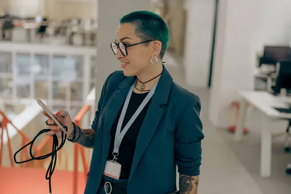 Stylish tattooed business woman with green short hair is use phone standing in modern office