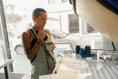 Bir atölyede baskı makinesi kullanırken ekran yazdırma filmi hazırlayan yaratıcı kadın işçiler