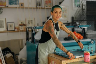 Cam sileceği olan kadın işçi, tasarım stüdyosunda çalışırken çerçeveye mürekkep basıyor. İpek ekran yazdırma