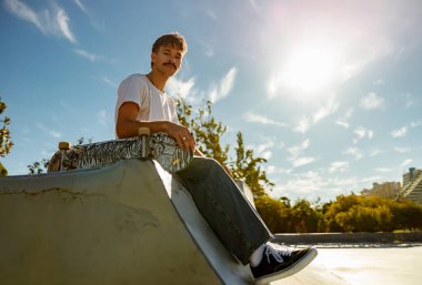 Mavi gökyüzüne karşı rampada kaykaylı genç erkek kaykaycı.