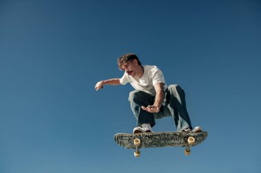 Aktif kaykaycı atlıyor ve kaykay parkında bir numara yapıyor.