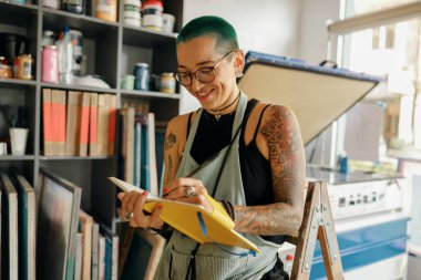 Gözlüklü kadın çalışan, atölyede çalışırken not defterine detayları sıralar. 