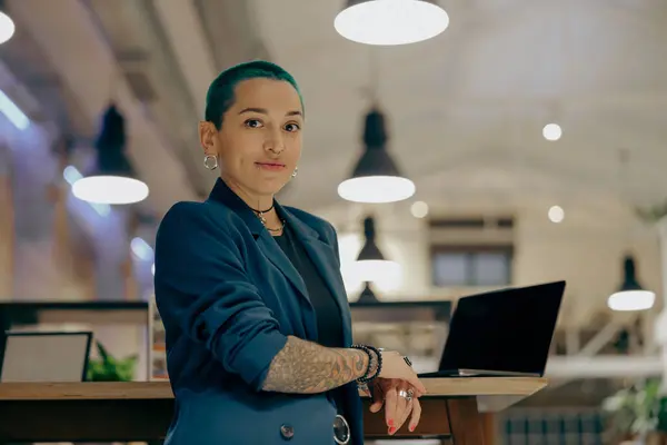 Portrait of stylish tattooed business woman with green short hair standing in modern office