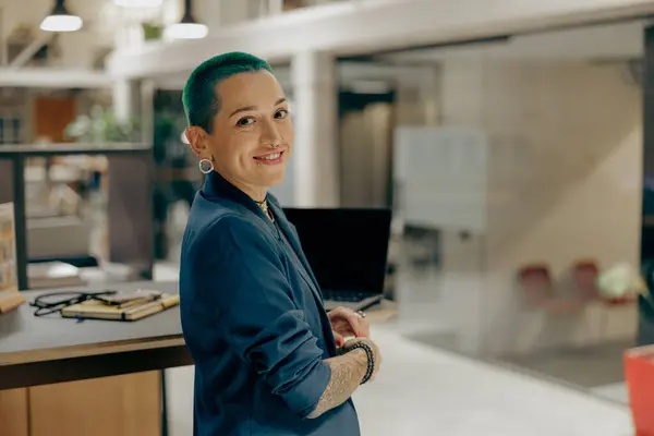 Portrait of creative tattooed female manager with green short hair on modern coworking background