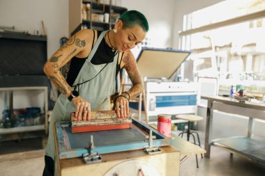 Cam sileceği olan kadın işçi, tasarım stüdyosunda çalışırken çerçeveye mürekkep basıyor. İpek ekran yazdırma