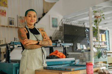 Tasarım stüdyosundaki parmak izi makinesinin arka planında duran gülümseyen kadın çalışan kameraya bakıyor.