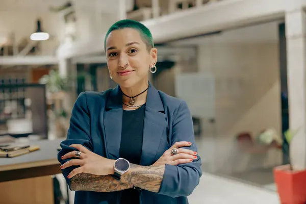 Portrait of stylish tattooed business woman with crossing hands standing in modern office