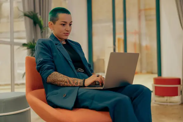 Creative tattooed business woman with green short hair working on laptop in modern office