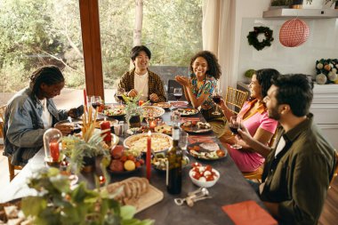 Bir grup gülen arkadaş evde Noel partisinde sohbet edip şarap içiyorlar.