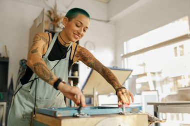 Cam sileceği olan kadın işçi, bir tasarım stüdyosunda ipekten ekran yöntemiyle tekstil üzerine resimler basıyor.