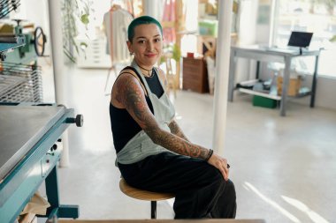 Tasarım stüdyosundaki baskı makinesinin arka planında oturan yaratıcı kadın işçi