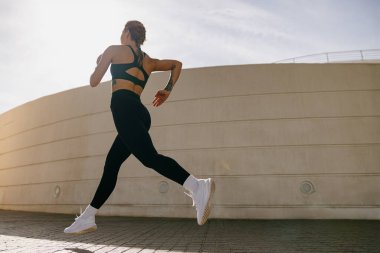 Spor giyim sektöründe formda bir bayan atlet modern binalarda koşuyor. Etkin yaşam tarzı kavramı