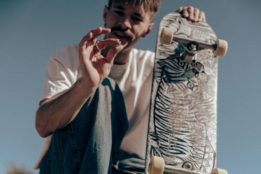 Erkek kaykaycı rampada kaykayla otururken bir şeye bakıyor. Yüksek kalite fotoğraf