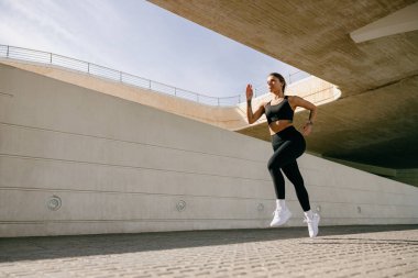 Aktif kadın atlet, modern bina arka planında sabah koşuyor. Sağlıklı yaşam konsepti