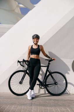 Güler yüzlü bisikletçi kadın dışarıda antrenman yaparken bisikletiyle dikiliyor. 