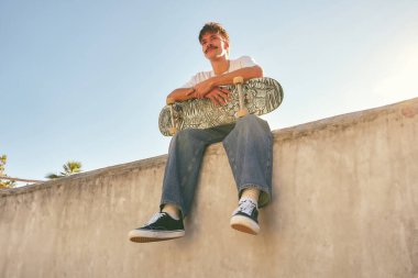 Genç kaykaycı kaykay parkının rampasında kaykayıyla oturuyor. Etkin yaşam tarzı kavramı