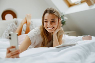 Güzel genç bir kadın bir yatakta uzanmış telefonuna bakıyor. Yüksek kalite