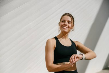 Spor kıyafetli gülümseyen kadın eğitimden sonra akıllı bakışlara bakıyor. Sabahları açık hava sporları.