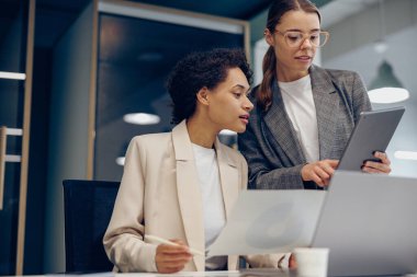 İki gülümseyen iş kadını bürodaki işi halletmek için belgelerle birlikte çalışıyorlar.